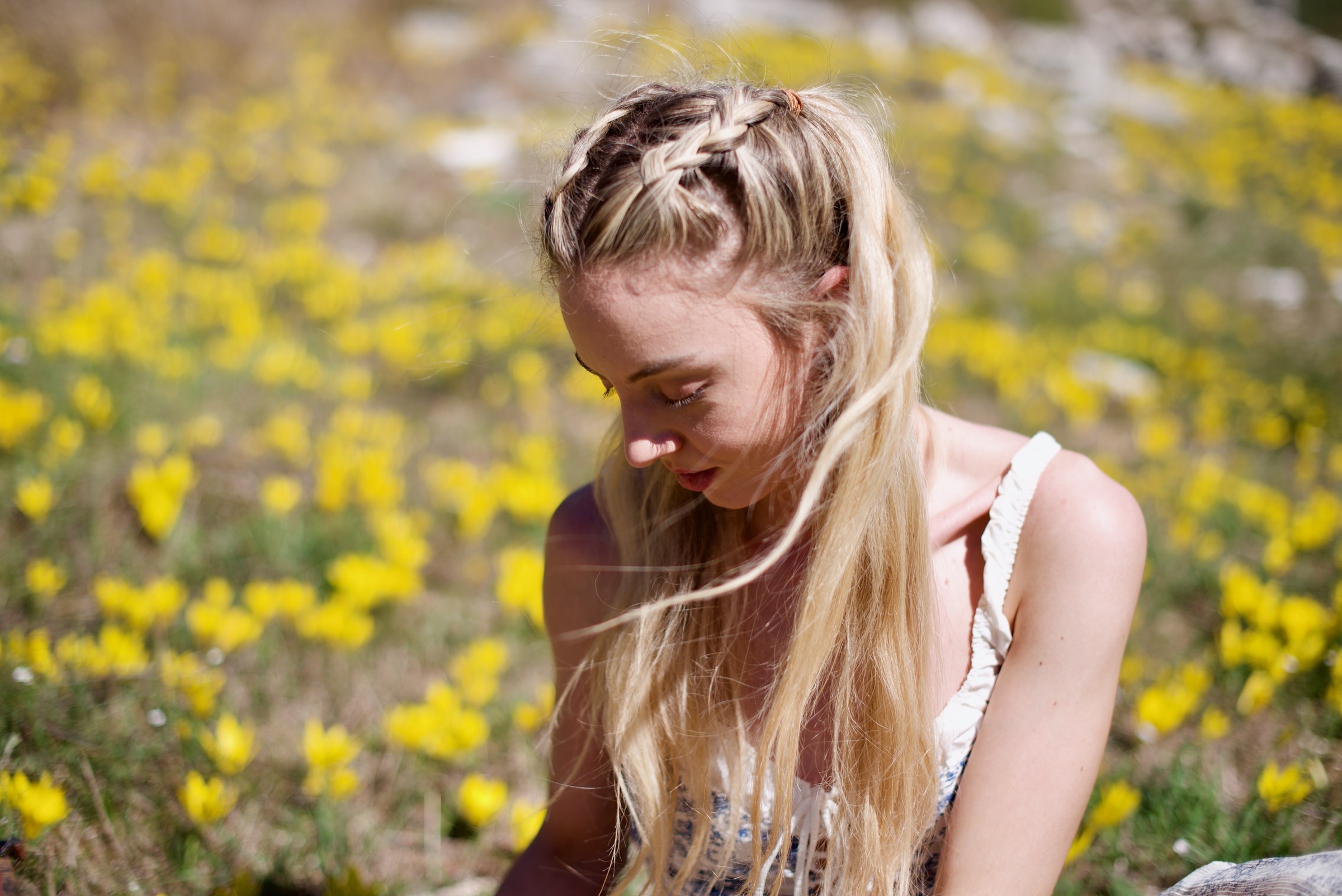 A woman with braided blonde hair sitting in a meadow full of small yellow flowers