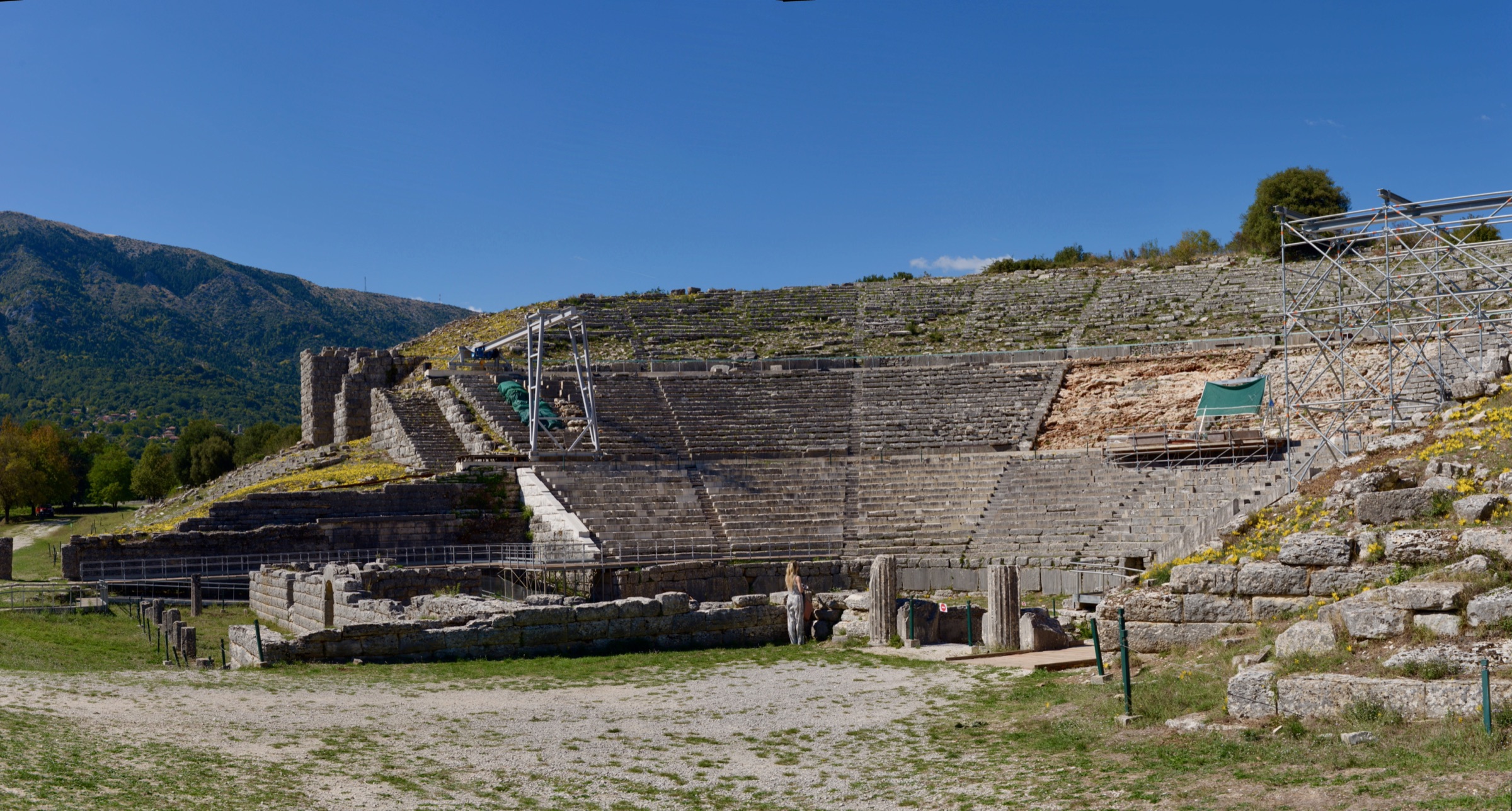 Panorama of the large stone theatre of Dodona under a blue sky, with restoration scaffolding on the right