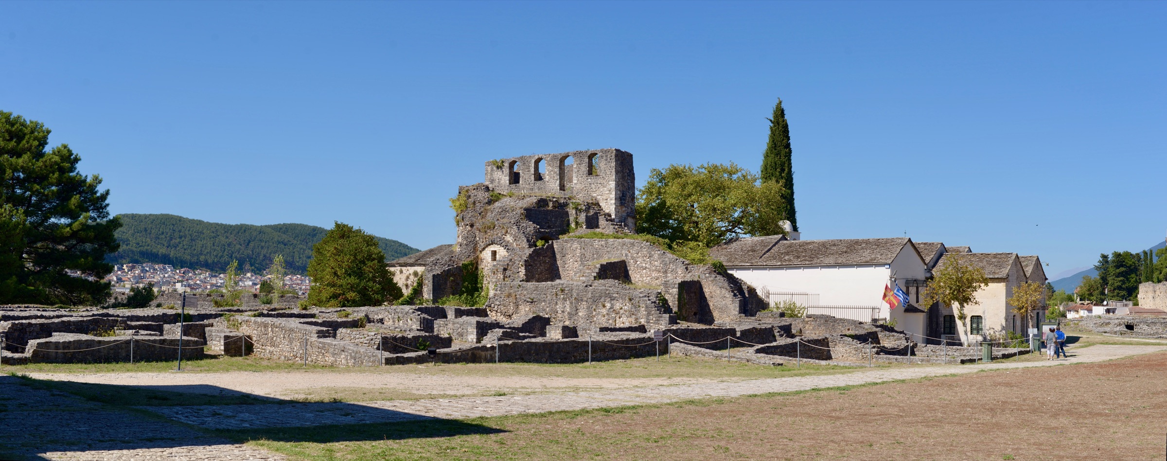 Stone ruins with arched windows inside the citadel of Ioannina, with a white museum building and the town behind