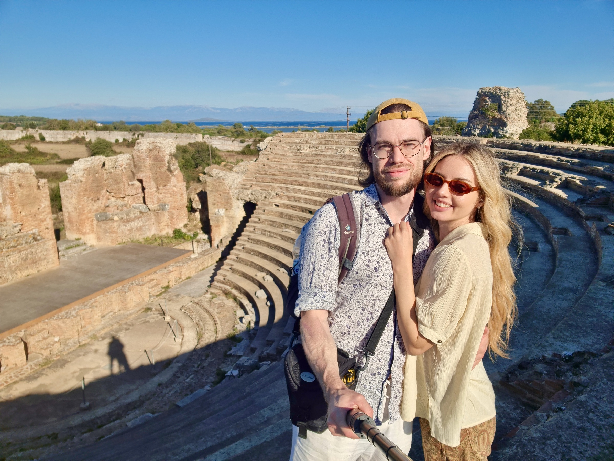 Selfie of a couple on the upper rows of the odeon, ruins and the sea behind them