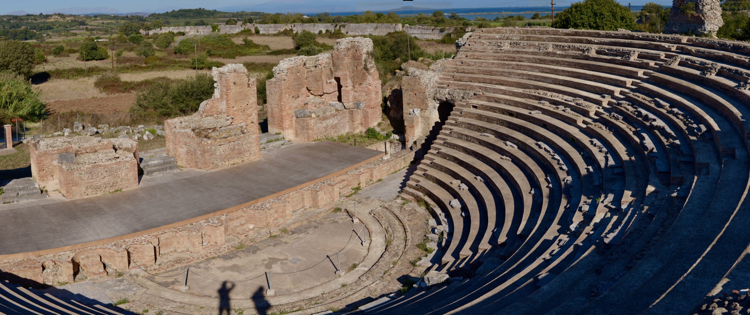 Panorama of the semicircular Roman odeon of Nikopolis with brick stage walls, two shadows on the orchestra