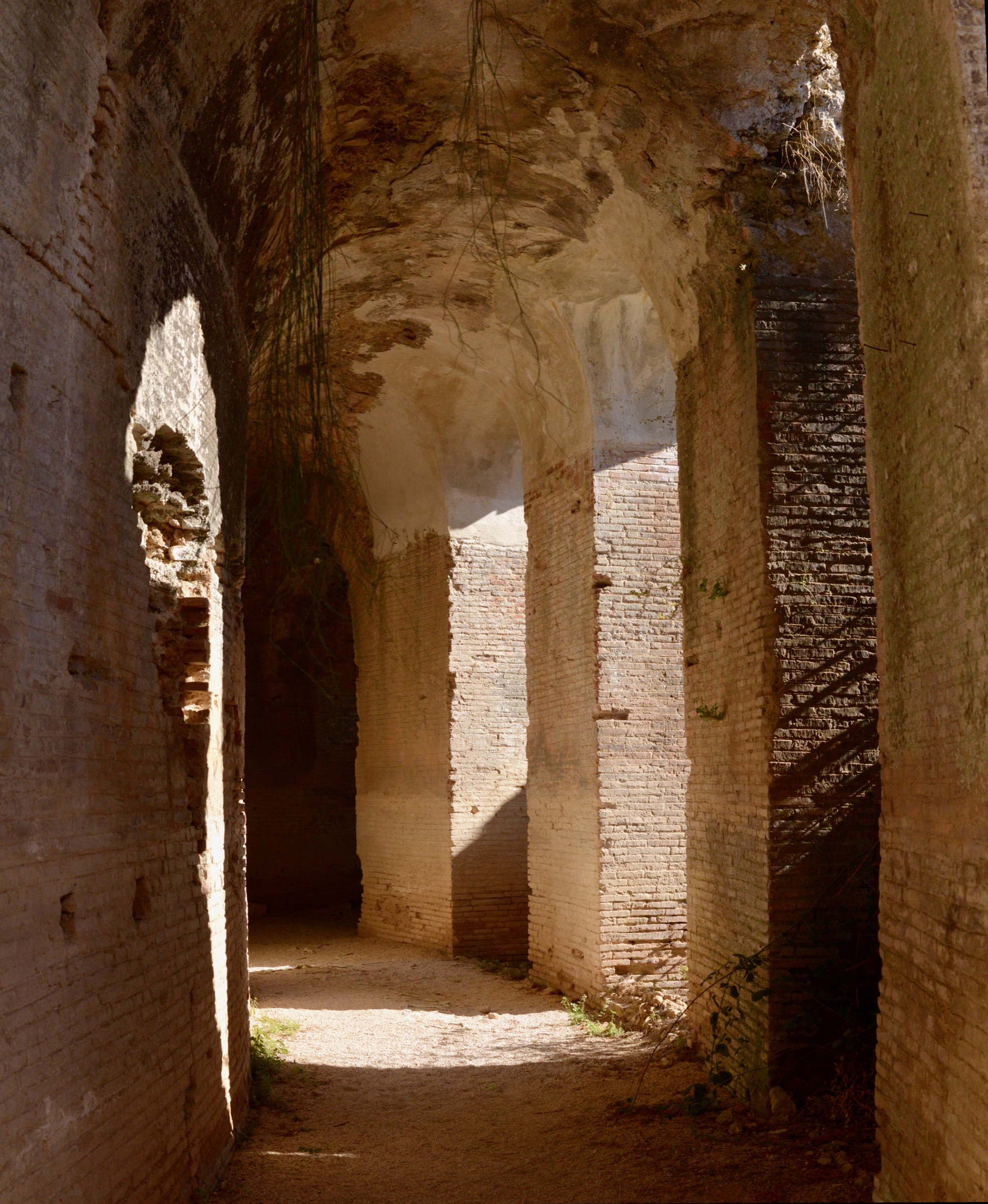 A vaulted brick corridor with sunlight falling through arches